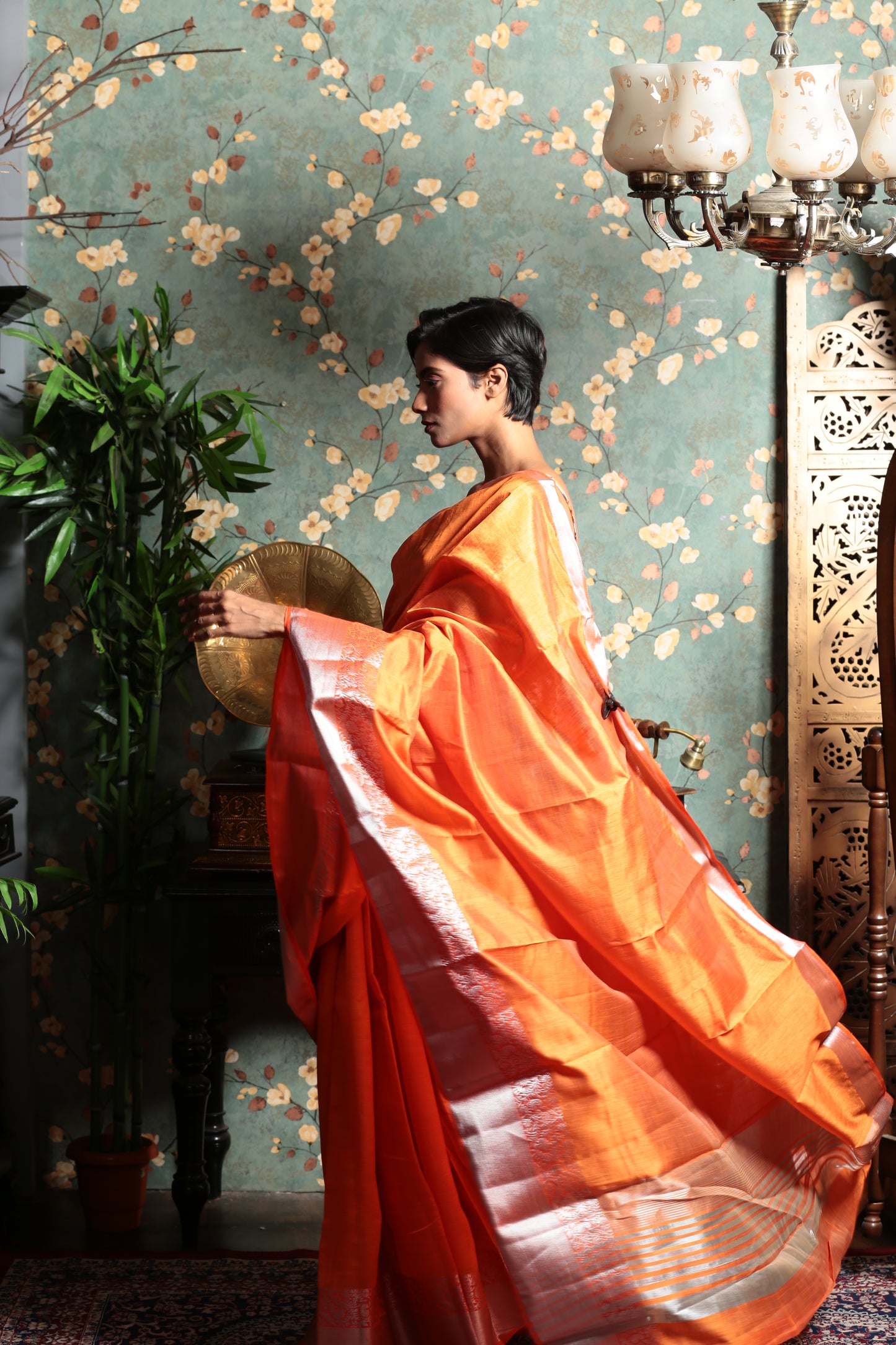 Bright orange raw silk saree with a shiny silver patterned border, perfect for evening wear | Urbane Essence
