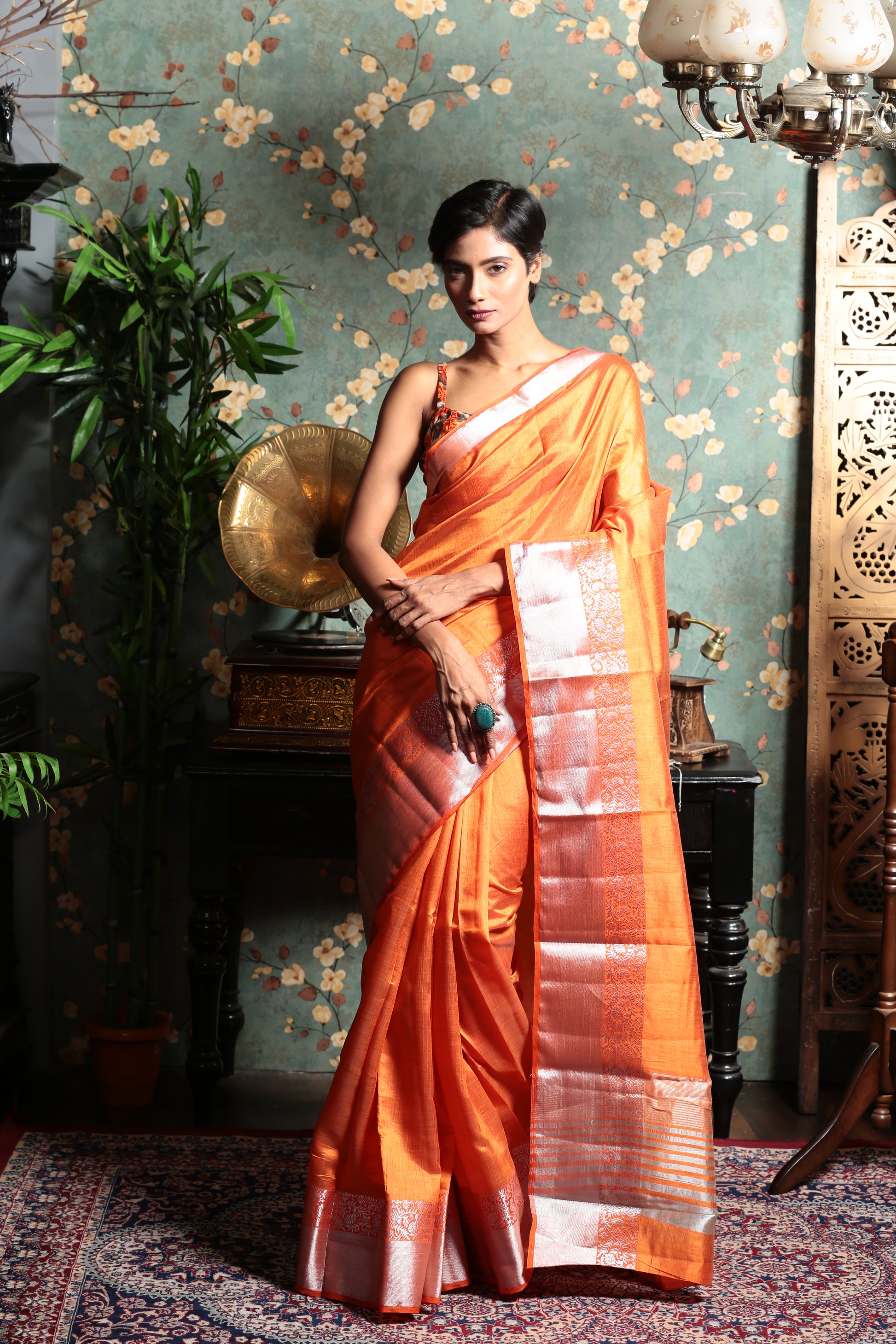 Bright orange raw silk saree with a shiny silver patterned border, perfect for evening wear | Urbane Essence