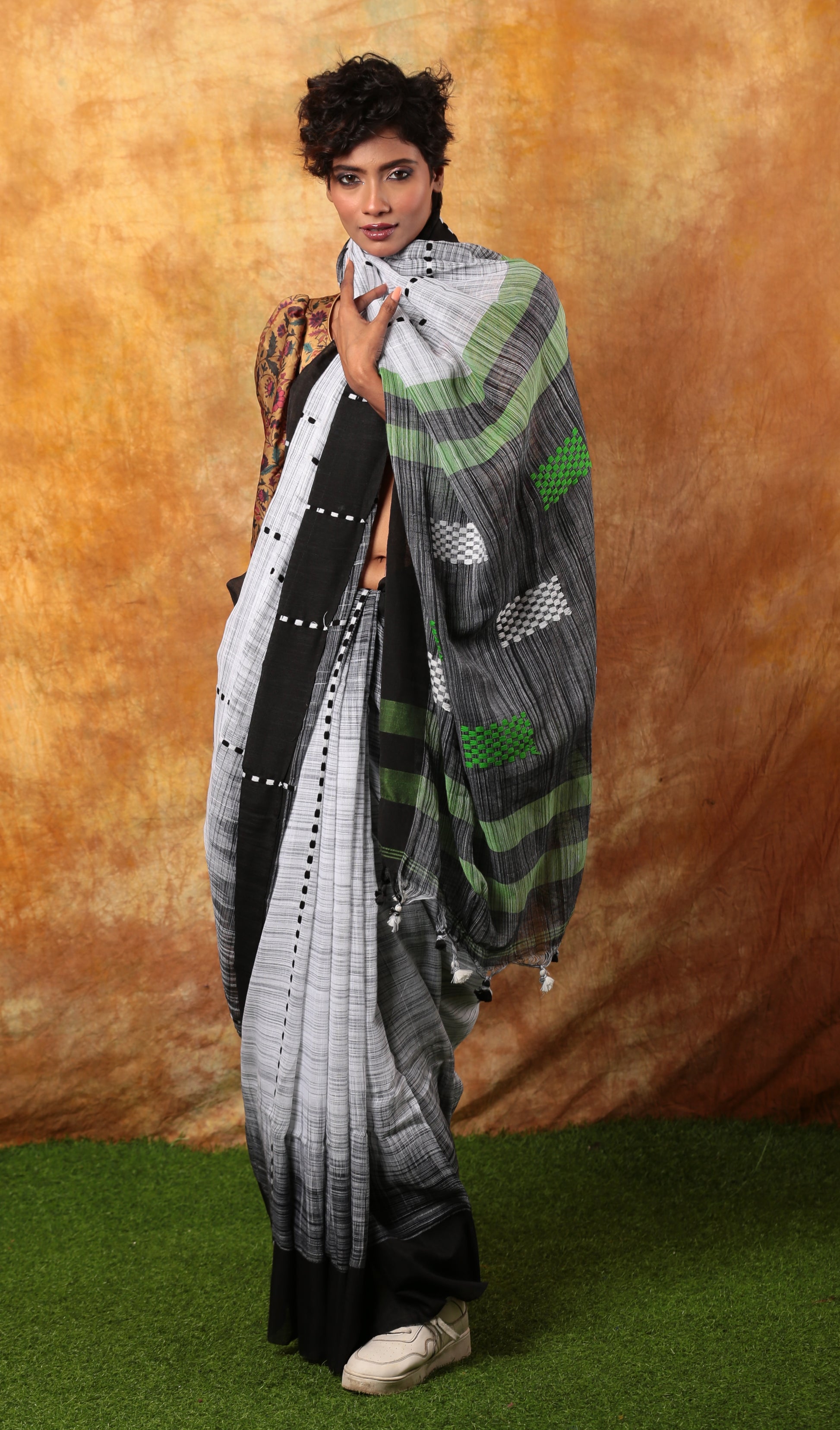 Model in a white and black Assam Khadi saree with traditional patterns and green striped pallu for summer occasions | Urbane Essence