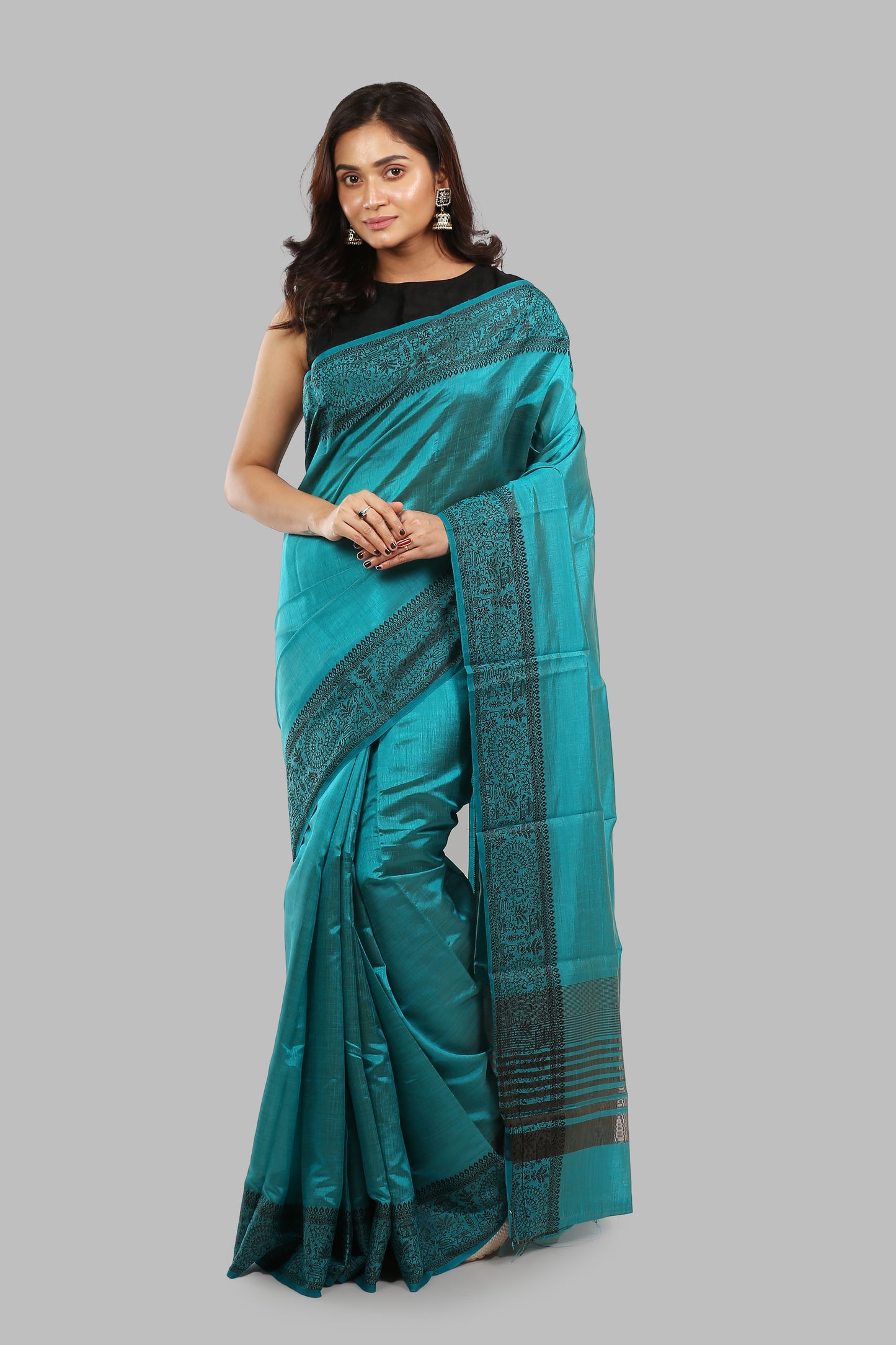 Woman in a teal raw silk saree with intricate black border patterns, suitable for traditional occasions | Urbane Essence