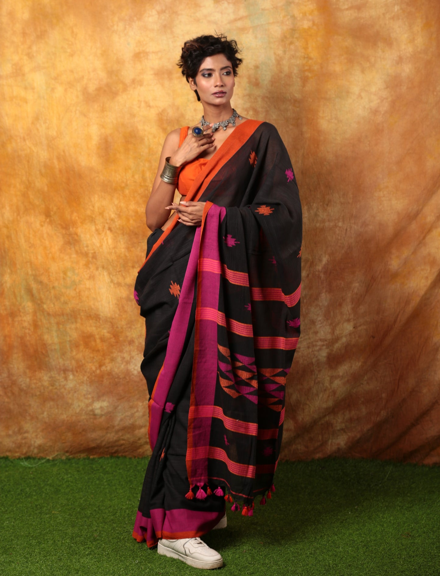 Black Assam Khadi saree with pink and orange border, intricate patterns, and tassels, perfect for festive occasions. | Urbane Essence
