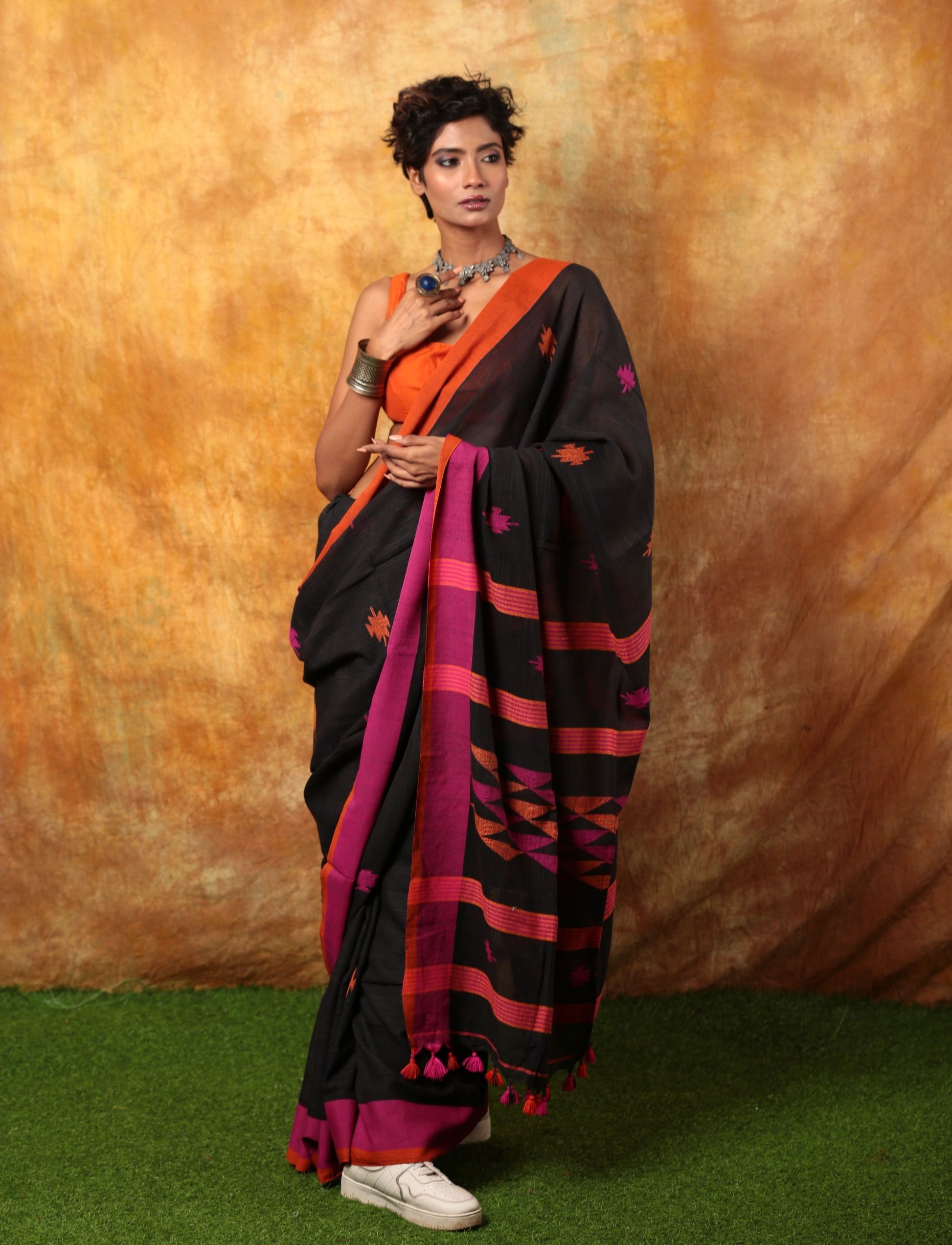 Black Assam Khadi saree with pink and orange border, intricate patterns, and tassels, perfect for festive occasions. | Urbane Essence